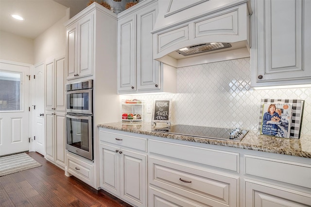 kitchen with dark wood-type flooring, tasteful backsplash, double oven, black electric stovetop, and white cabinets