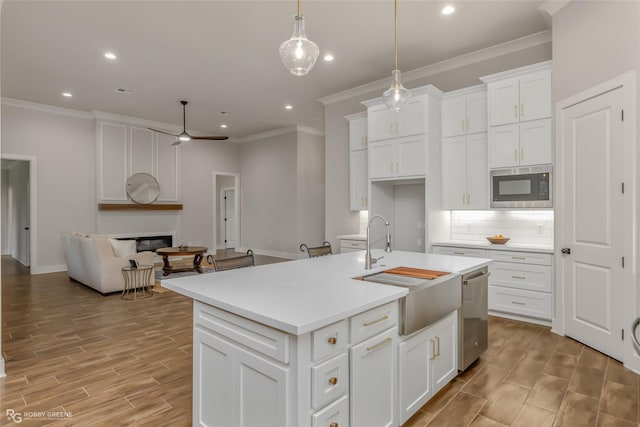 kitchen with decorative light fixtures, built in microwave, dishwasher, white cabinets, and a center island with sink