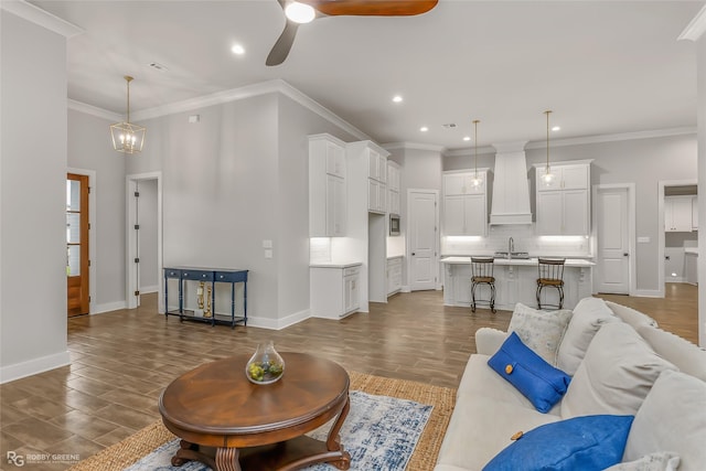 living room featuring ornamental molding, sink, and ceiling fan with notable chandelier