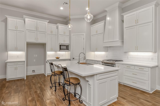 kitchen featuring stainless steel appliances, sink, a center island with sink, and white cabinets