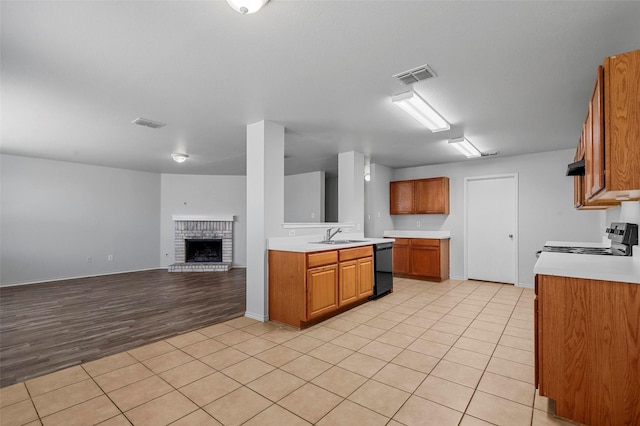 kitchen featuring sink, black dishwasher, stainless steel range, a fireplace, and light tile patterned flooring