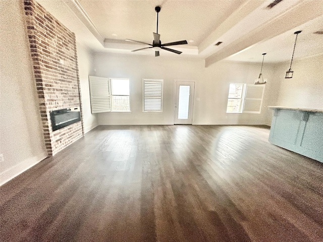 unfurnished living room featuring dark wood-type flooring, ceiling fan, heating unit, a tray ceiling, and a fireplace