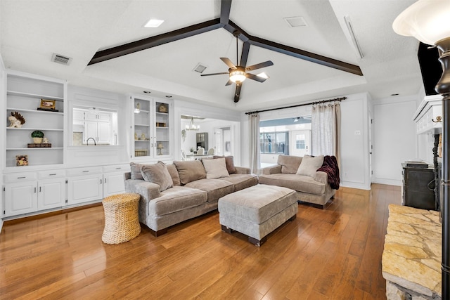 living room featuring lofted ceiling with beams, ceiling fan with notable chandelier, built in shelves, and light hardwood / wood-style floors