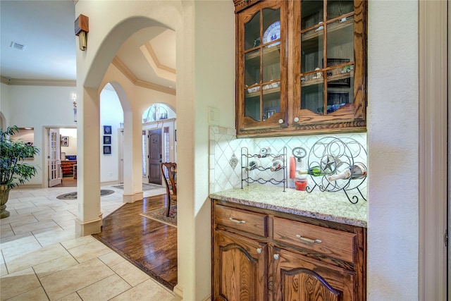 bar featuring tasteful backsplash, ornamental molding, and light stone countertops