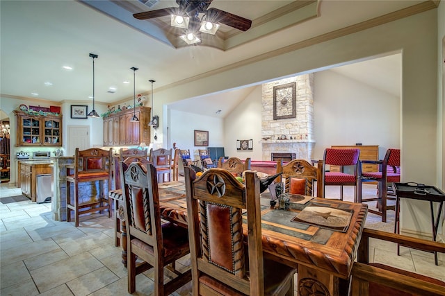 dining space featuring a raised ceiling, ornamental molding, a stone fireplace, and ceiling fan