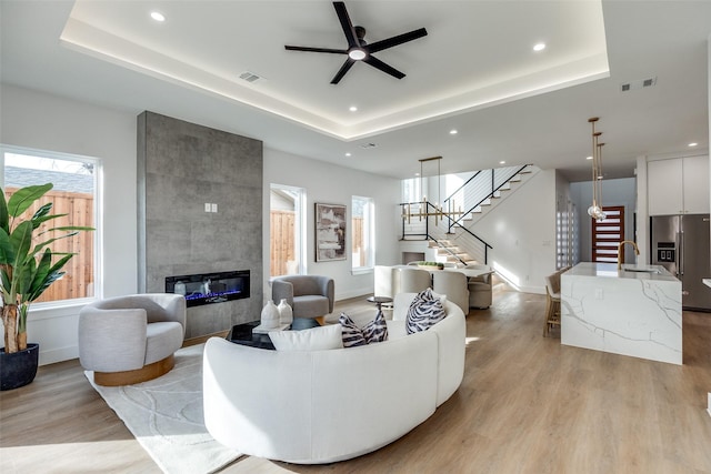 living room featuring a fireplace, a raised ceiling, sink, and light hardwood / wood-style flooring