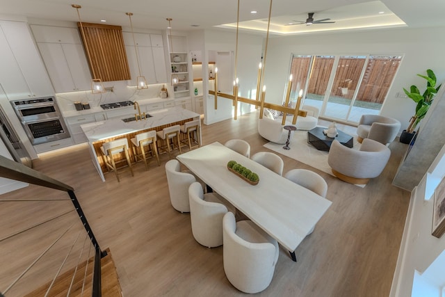 dining space with sink, light hardwood / wood-style floors, and a raised ceiling