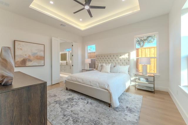 bedroom featuring light wood-type flooring, a raised ceiling, ceiling fan, and ensuite bathroom