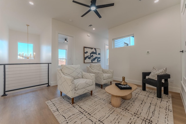 living room featuring ceiling fan with notable chandelier and light wood-type flooring