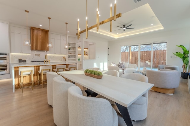 dining room featuring a raised ceiling, ceiling fan, and light hardwood / wood-style floors