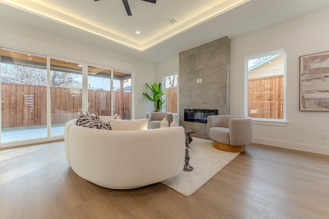 living room with ceiling fan, a fireplace, a raised ceiling, and light wood-type flooring