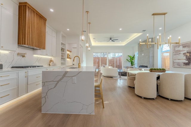 kitchen with white cabinetry, sink, hanging light fixtures, a large island, and light hardwood / wood-style flooring