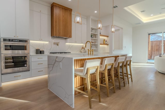 kitchen featuring white cabinetry, stainless steel double oven, and a center island with sink