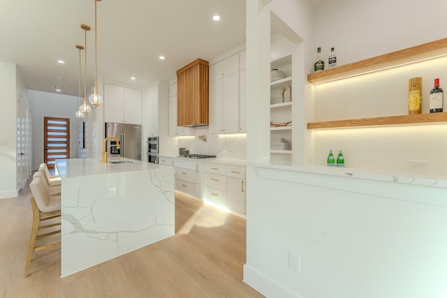 kitchen with pendant lighting, white cabinetry, stainless steel appliances, and a center island with sink