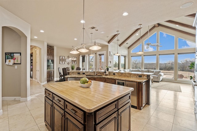 kitchen featuring a spacious island, sink, decorative light fixtures, beamed ceiling, and a healthy amount of sunlight