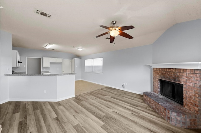 unfurnished living room with vaulted ceiling, ceiling fan, a brick fireplace, a textured ceiling, and light hardwood / wood-style flooring