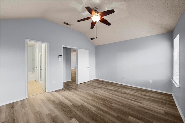 unfurnished bedroom featuring ceiling fan, ensuite bathroom, light hardwood / wood-style floors, a textured ceiling, and vaulted ceiling