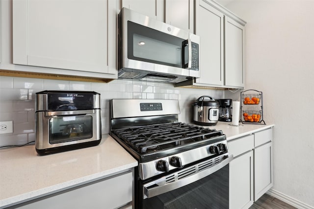 kitchen with tasteful backsplash, white cabinets, hardwood / wood-style flooring, light stone counters, and stainless steel appliances