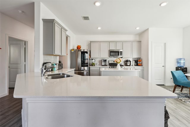 kitchen with sink, gray cabinetry, light hardwood / wood-style flooring, appliances with stainless steel finishes, and decorative backsplash