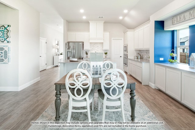 kitchen featuring appliances with stainless steel finishes, white cabinetry, an island with sink, decorative backsplash, and light wood-type flooring