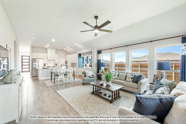 living room with a wealth of natural light, vaulted ceiling, ceiling fan, and light wood-type flooring