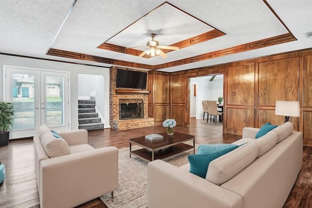 living room featuring french doors, a brick fireplace, wooden walls, a tray ceiling, and hardwood / wood-style flooring