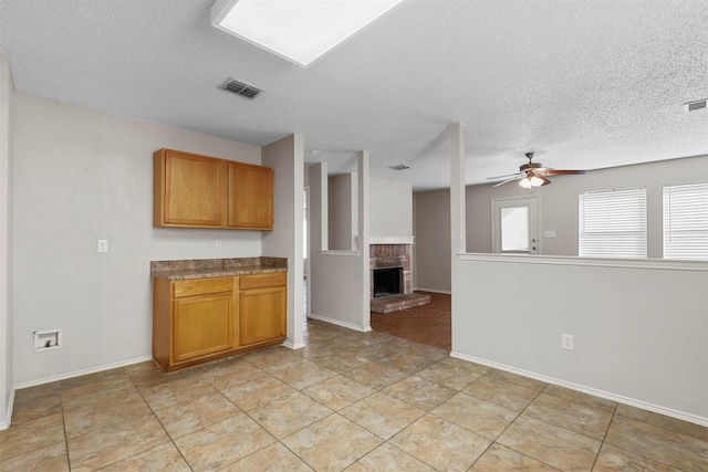 kitchen with ceiling fan, a fireplace, a textured ceiling, and light tile patterned floors