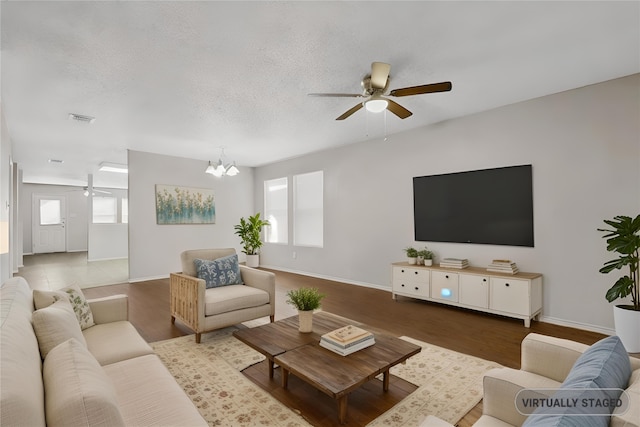 living room with wood-type flooring, ceiling fan with notable chandelier, and a textured ceiling