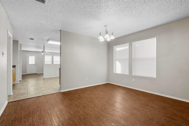 unfurnished room with ceiling fan with notable chandelier, light hardwood / wood-style flooring, and a textured ceiling