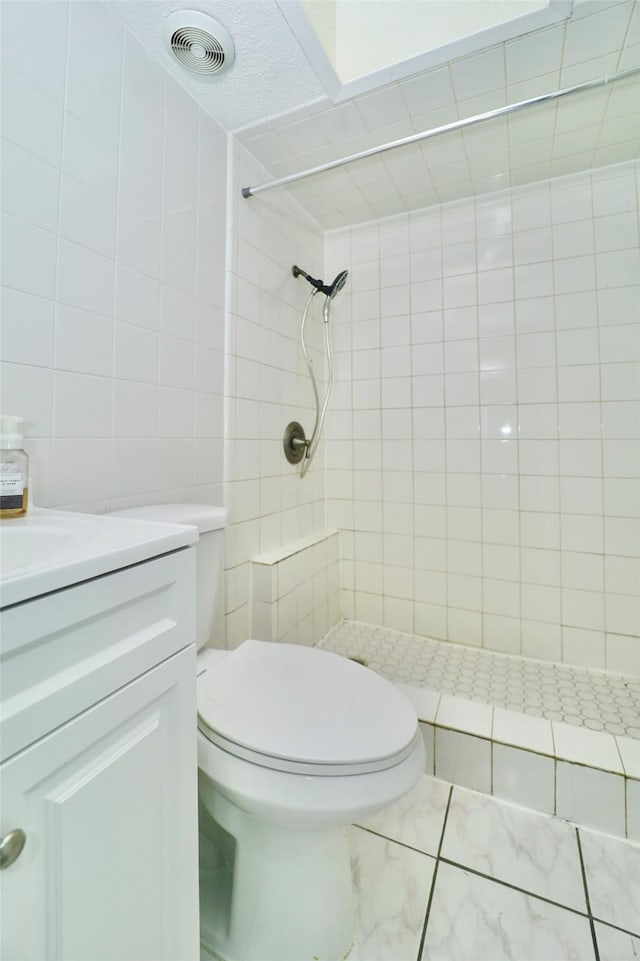 bathroom featuring tile walls, vanity, tiled shower, toilet, and a textured ceiling