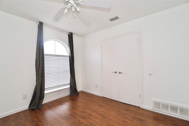 unfurnished bedroom featuring multiple windows, dark wood-type flooring, ceiling fan, and a closet