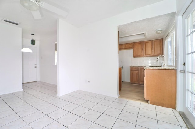 kitchen featuring sink, light stone counters, light tile patterned floors, ceiling fan, and backsplash