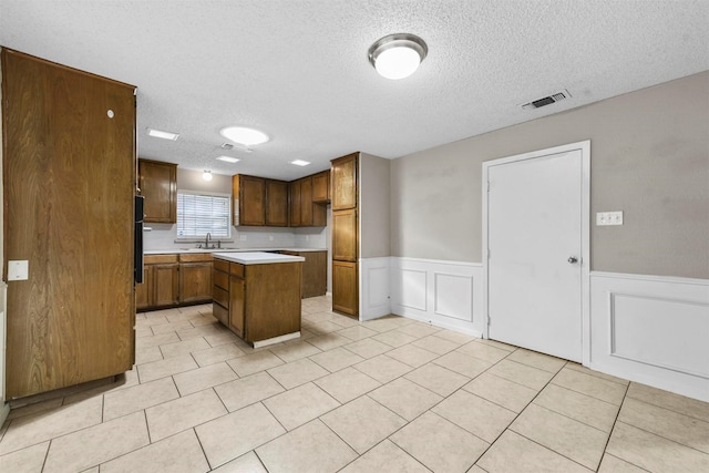 kitchen featuring sink, a center island, a textured ceiling, and light tile patterned flooring