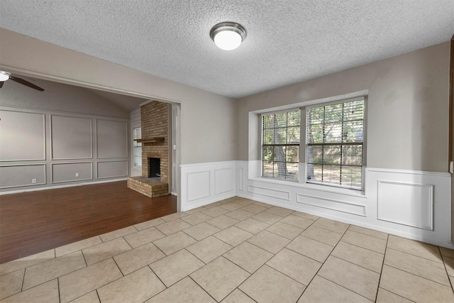 unfurnished living room with ceiling fan, a brick fireplace, light tile patterned floors, and a textured ceiling