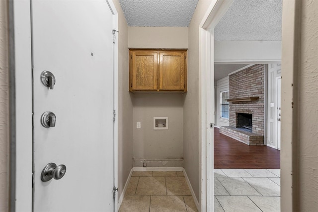 interior space with light tile patterned flooring, cabinets, a brick fireplace, a textured ceiling, and washer hookup