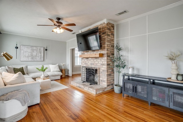 living room with hardwood / wood-style floors, ornamental molding, a brick fireplace, and ceiling fan