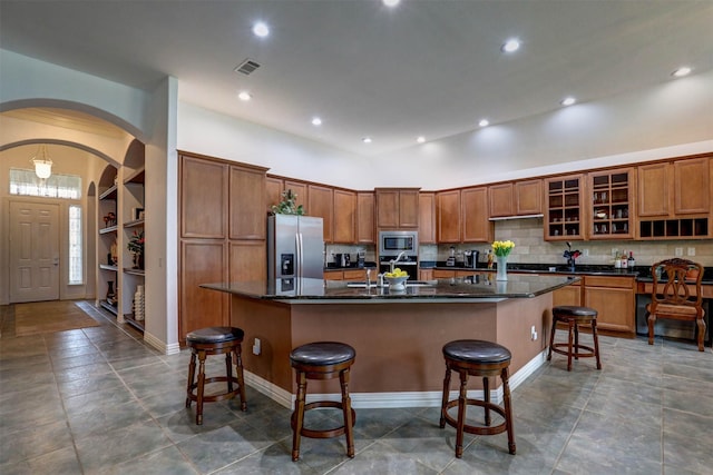 kitchen with a breakfast bar, tasteful backsplash, dark stone countertops, a kitchen island with sink, and stainless steel appliances