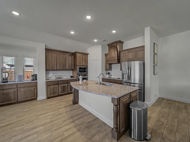 kitchen with sink, light stone counters, light wood-type flooring, stainless steel appliances, and a kitchen island with sink