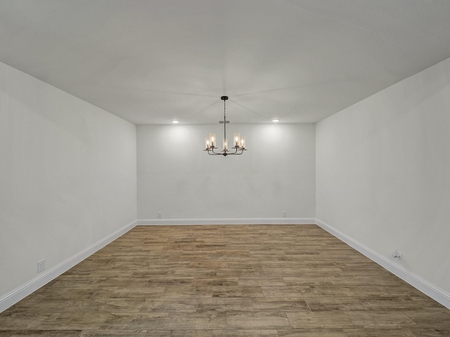 empty room with hardwood / wood-style floors and a notable chandelier