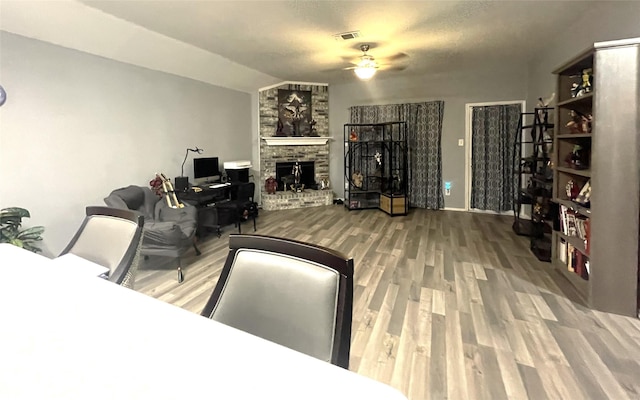 living room with ceiling fan, a large fireplace, wood-type flooring, and vaulted ceiling