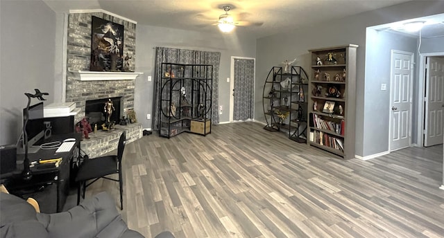 office area with ceiling fan, wood-type flooring, and a brick fireplace