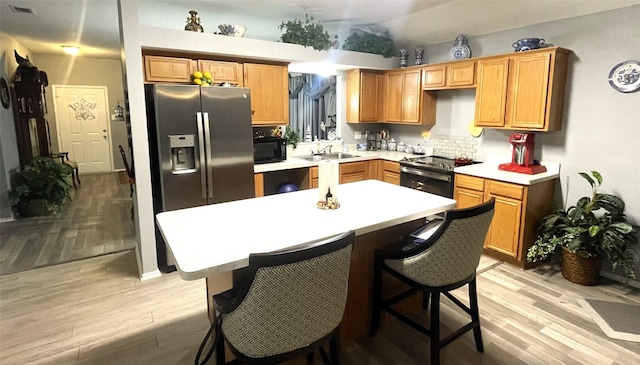 kitchen featuring stainless steel appliances, a kitchen island, sink, and light wood-type flooring