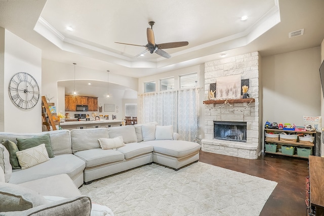 living room with a fireplace, concrete floors, ornamental molding, ceiling fan, and a tray ceiling