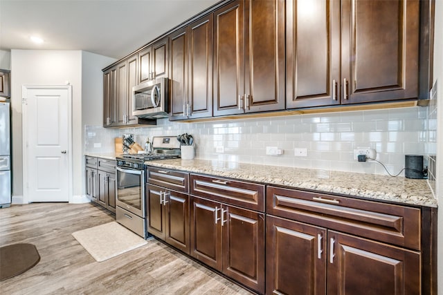 kitchen with dark brown cabinets, light hardwood / wood-style flooring, stainless steel appliances, light stone countertops, and backsplash