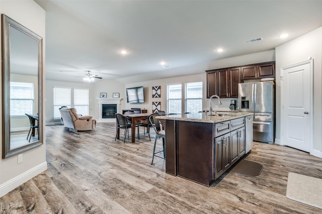 kitchen featuring a kitchen breakfast bar, stainless steel refrigerator with ice dispenser, dark brown cabinetry, a healthy amount of sunlight, and a center island with sink