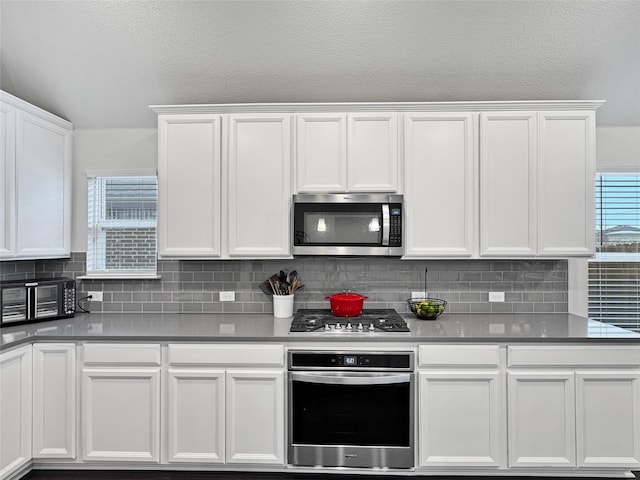 kitchen featuring lofted ceiling, appliances with stainless steel finishes, white cabinets, and backsplash