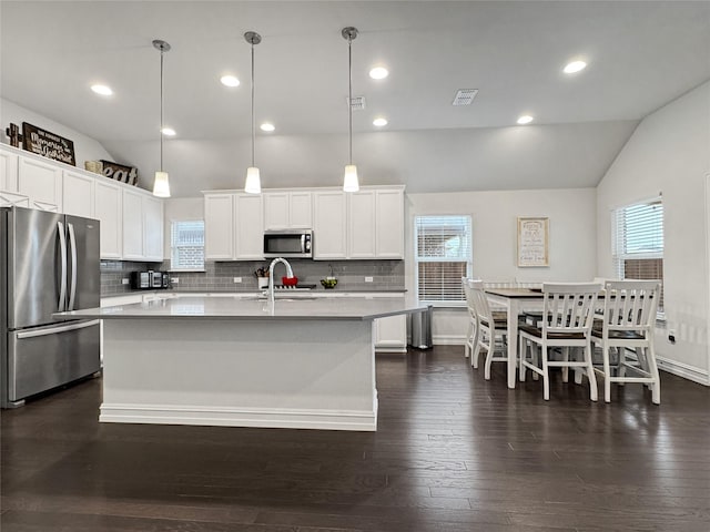 kitchen with vaulted ceiling, appliances with stainless steel finishes, white cabinets, hanging light fixtures, and a center island with sink