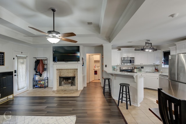 kitchen with appliances with stainless steel finishes, a tray ceiling, a breakfast bar area, and white cabinets