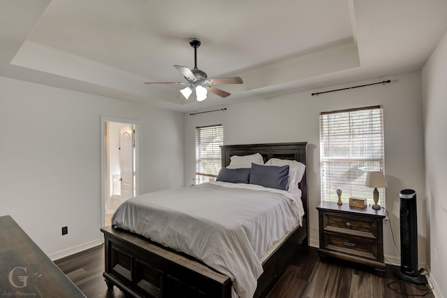 bedroom with a raised ceiling, dark hardwood / wood-style floors, connected bathroom, and ceiling fan