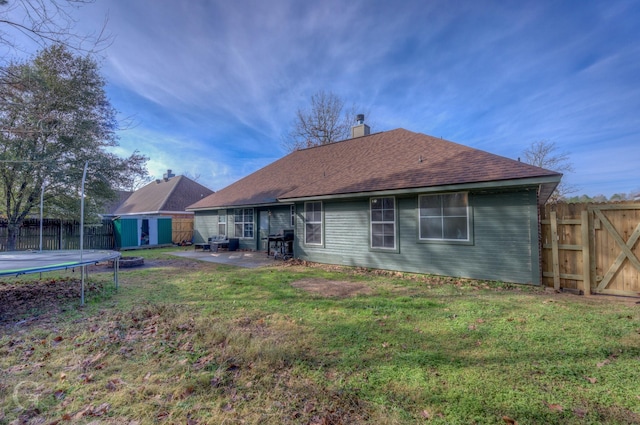 back of house featuring a trampoline, a lawn, a patio, and a shed